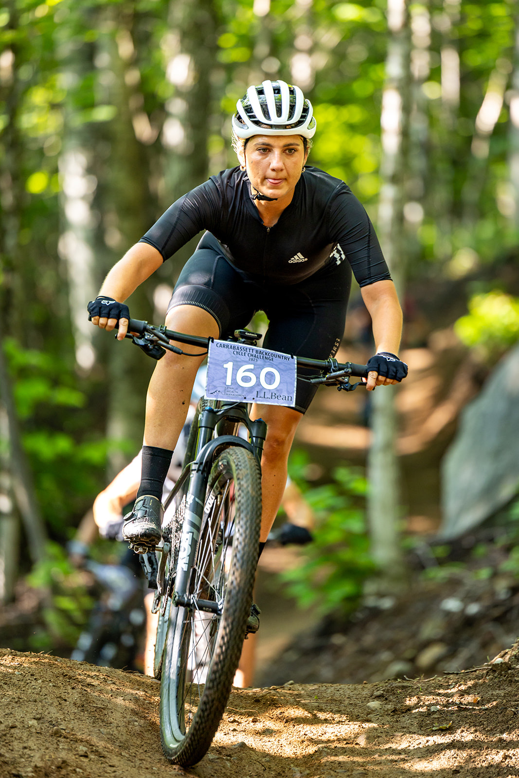 Racer in a black kit climbing a rooty forest trail