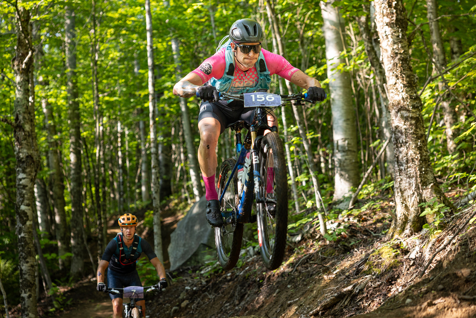 Racer in a pink jersey catching air on a forest trail