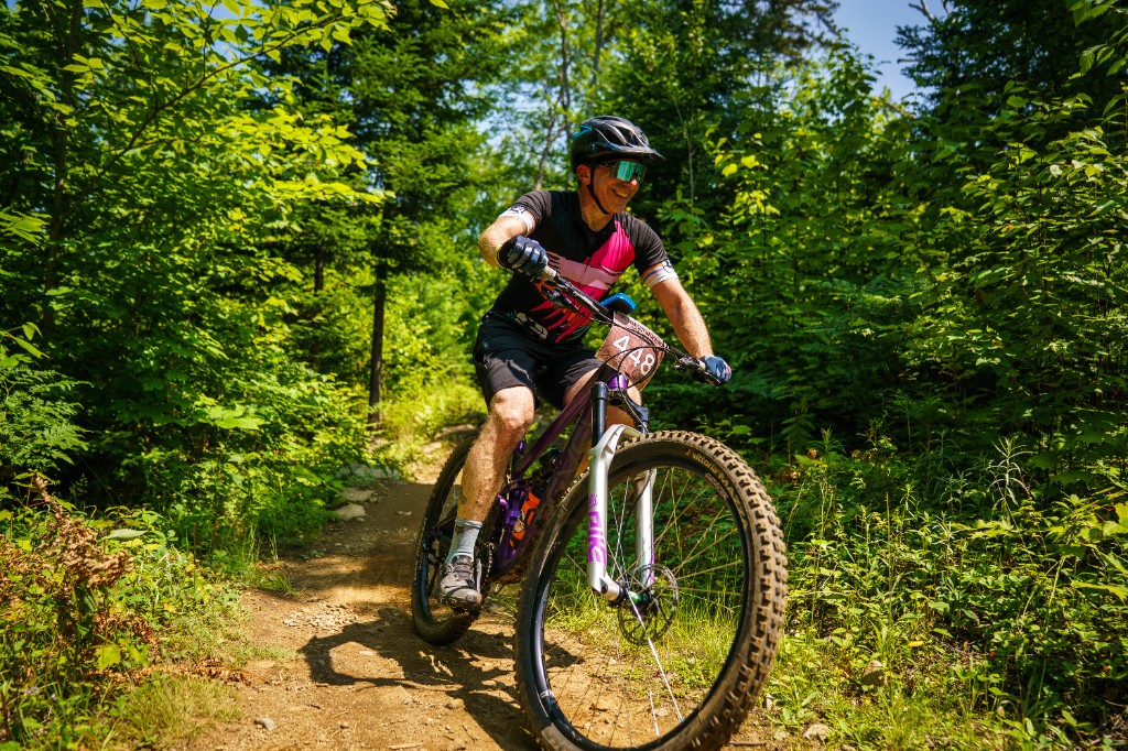 Smiling racer carving through sunlit forest singletrack